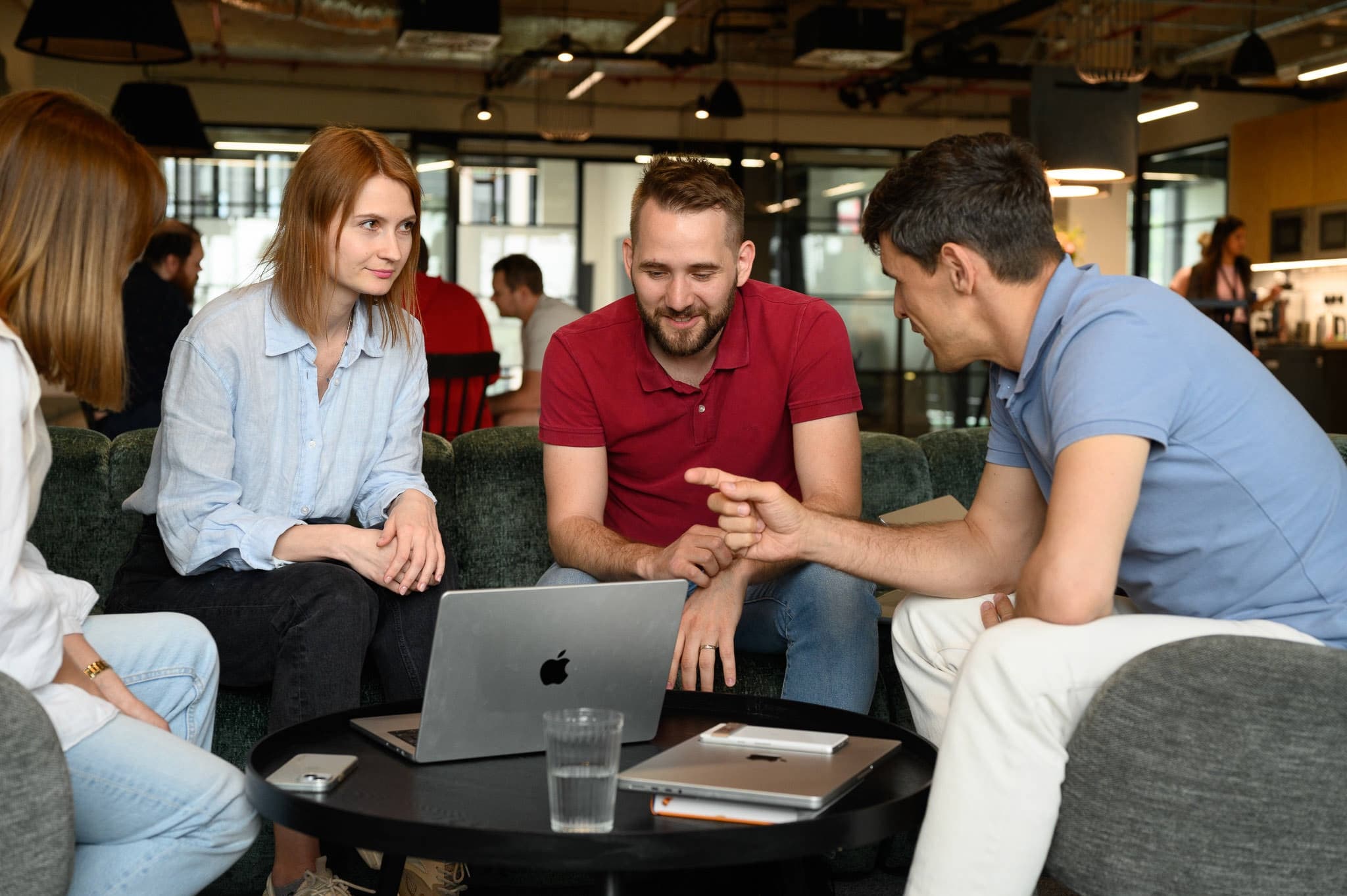 Four colleagues sitting on a sofa around a laptop, discussing a project together in a modern office space.