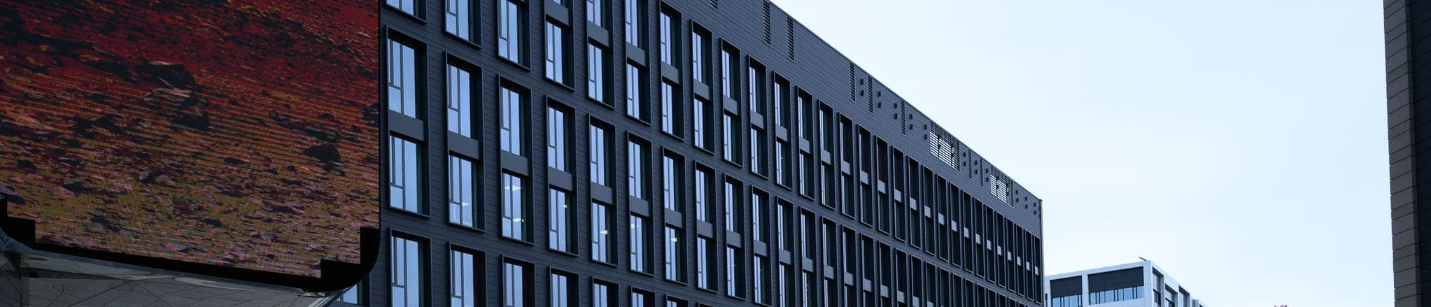 Exterior view of a modern office building with tall windows, partially covered by a large digital screen.
